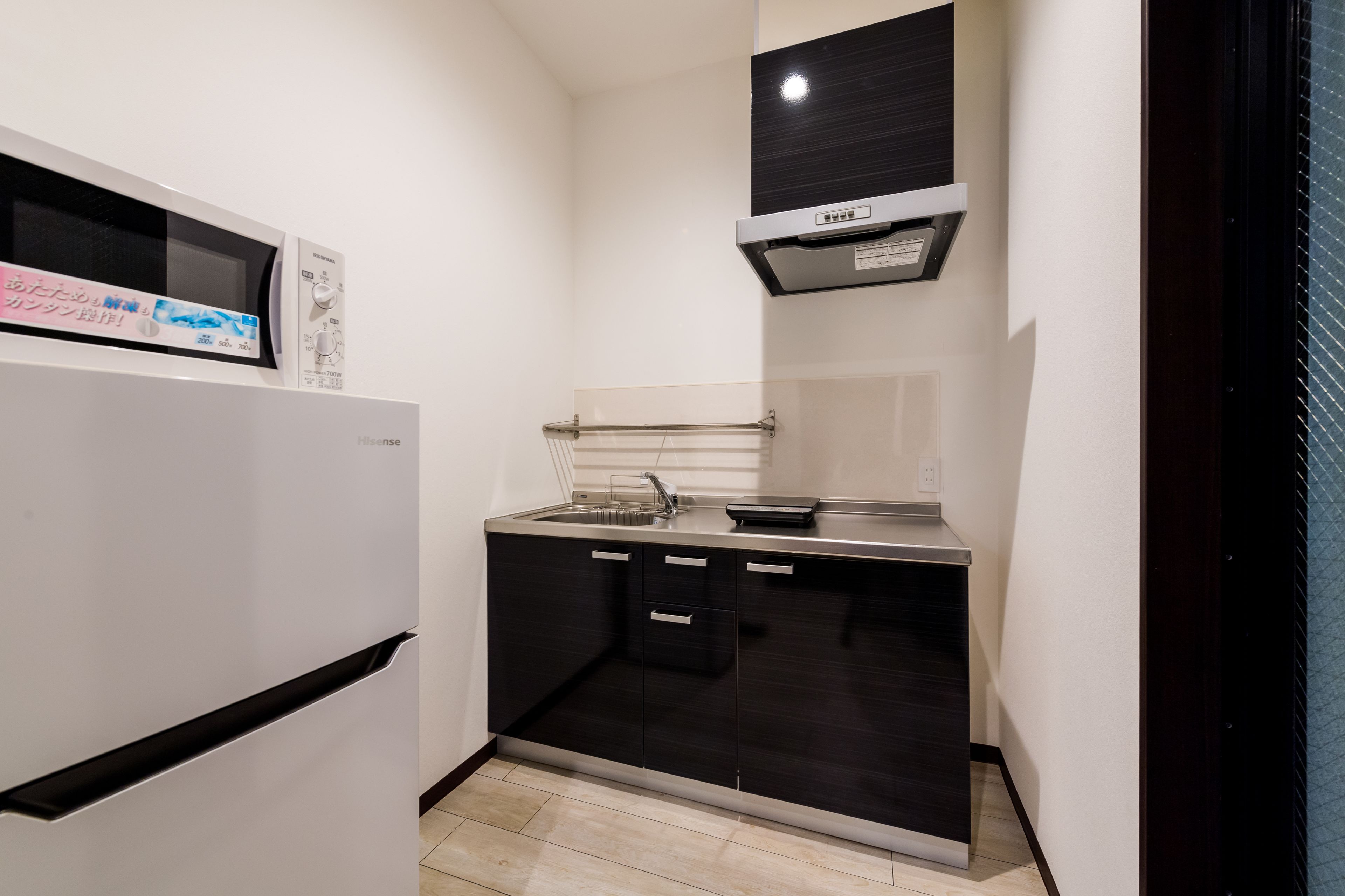 A compact kitchen with a white refrigerator, black cabinets, a stainless steel countertop, and a black range hood.