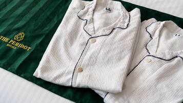 Two neatly folded white shirts with dark piping and buttons on a green striped bedspread.