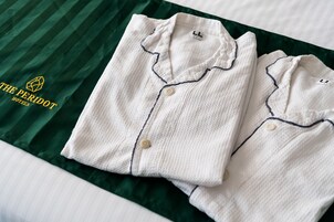 Dos camisas blancas, bien dobladas, con ribetes y botones oscuros sobre una colcha verde a rayas.