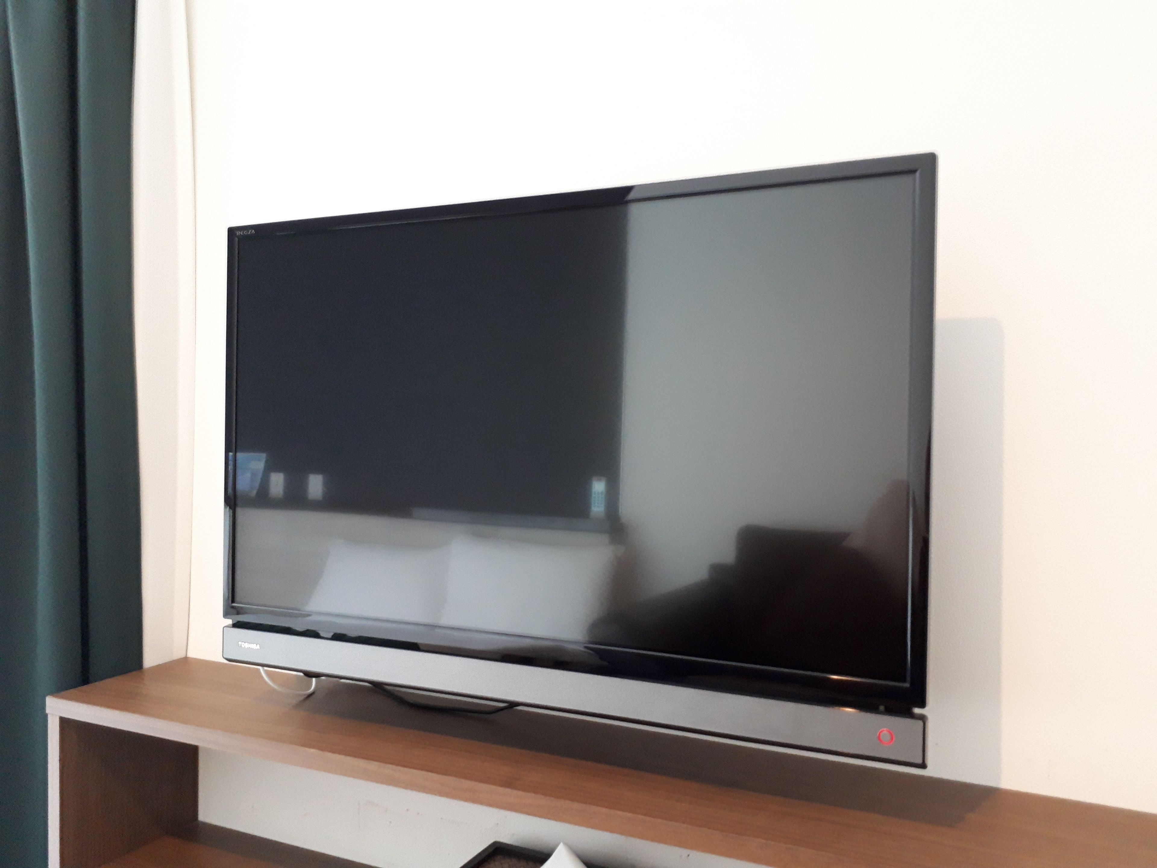 Un televisor de pantalla plana sobre un atril de madera frente a una pared lisa.