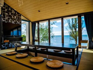 A modern room with a large wooden table, tatami mats, and a TV on the wall. - THE PERIDOT Smart Hotel Tancha Ward (Onna)