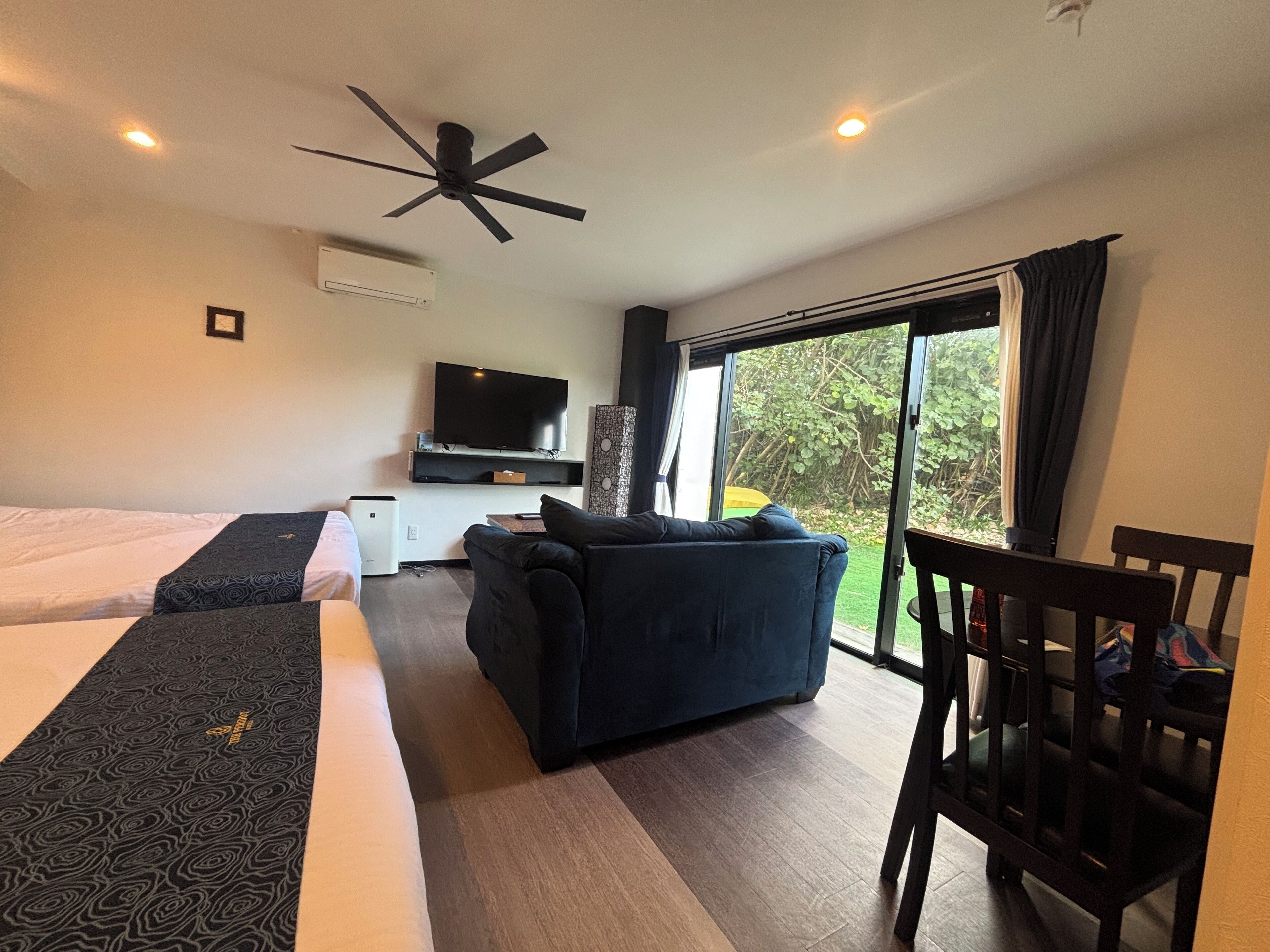 A modern hotel room with a bed, a sofa, a TV, and a ceiling fan.