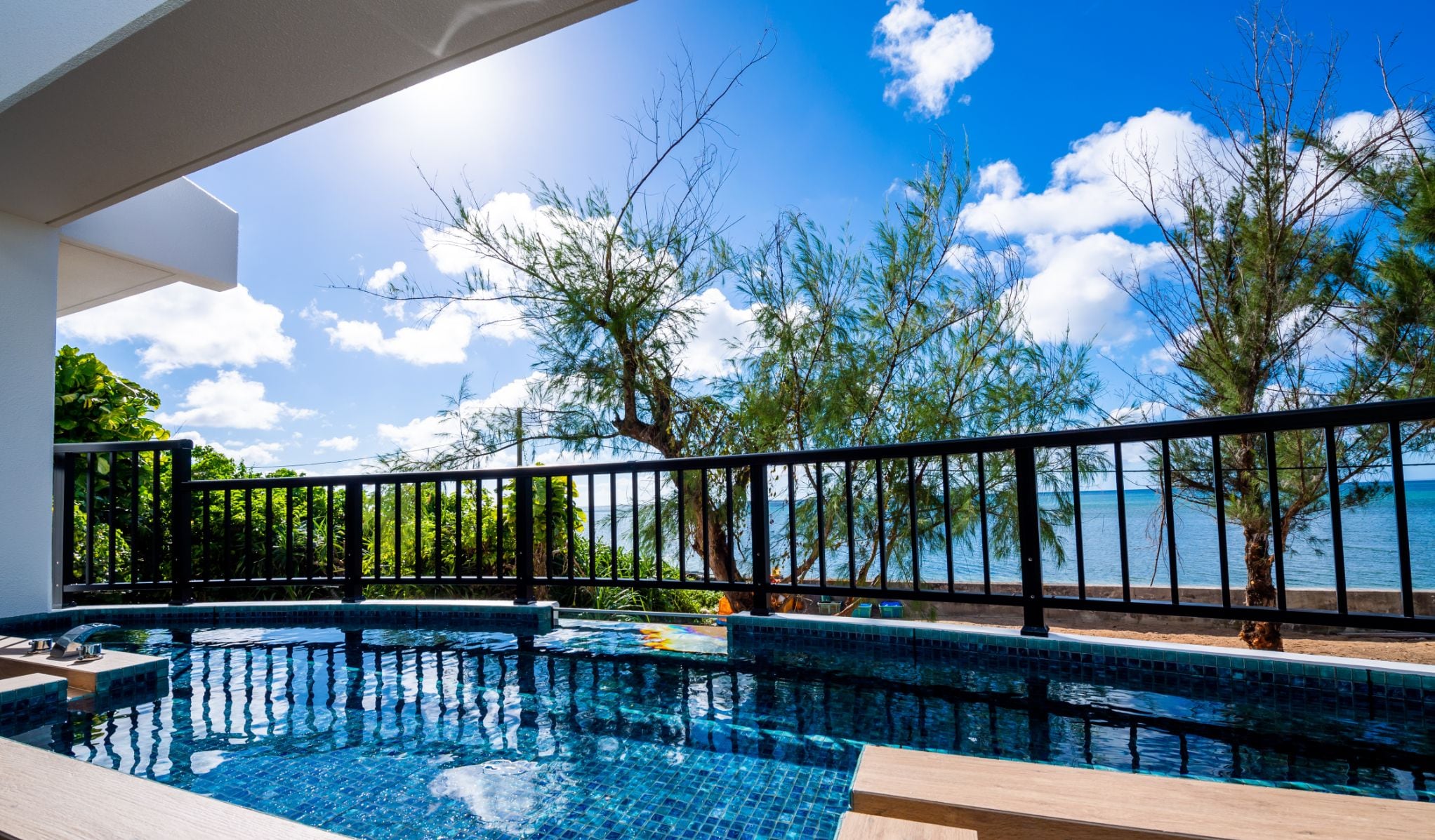 A private pool with a view of the sea and trees, surrounded by a black metal fence.