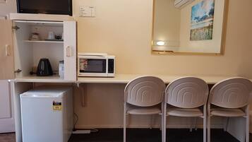 A compact kitchenette with a microwave, kettle, and small fridge. There are two chairs and a large mirror above the counter.