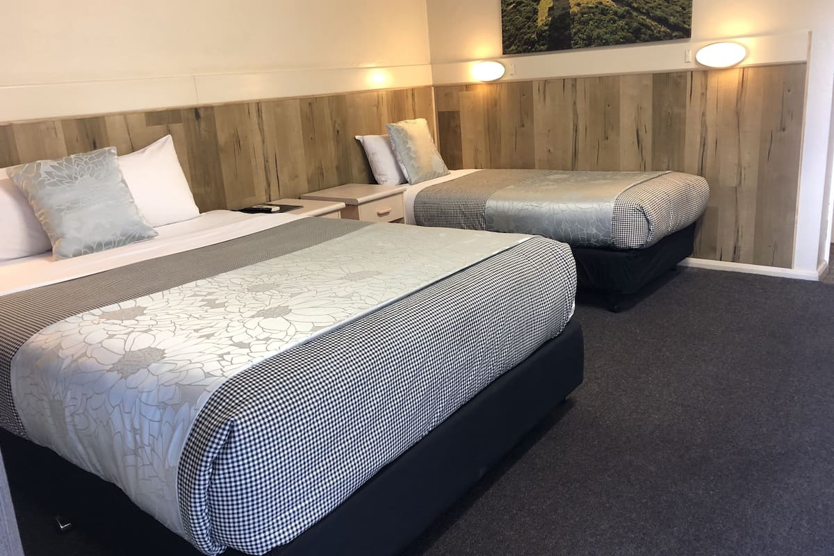 A hotel room with two beds, a wooden headboard, a nightstand, a lamp, and a wall-mounted picture.