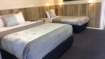 Una habitación de hotel con dos camas, un cabecero de madera, una mesita de noche, una lámpara y un cuadro colgado en la pared.