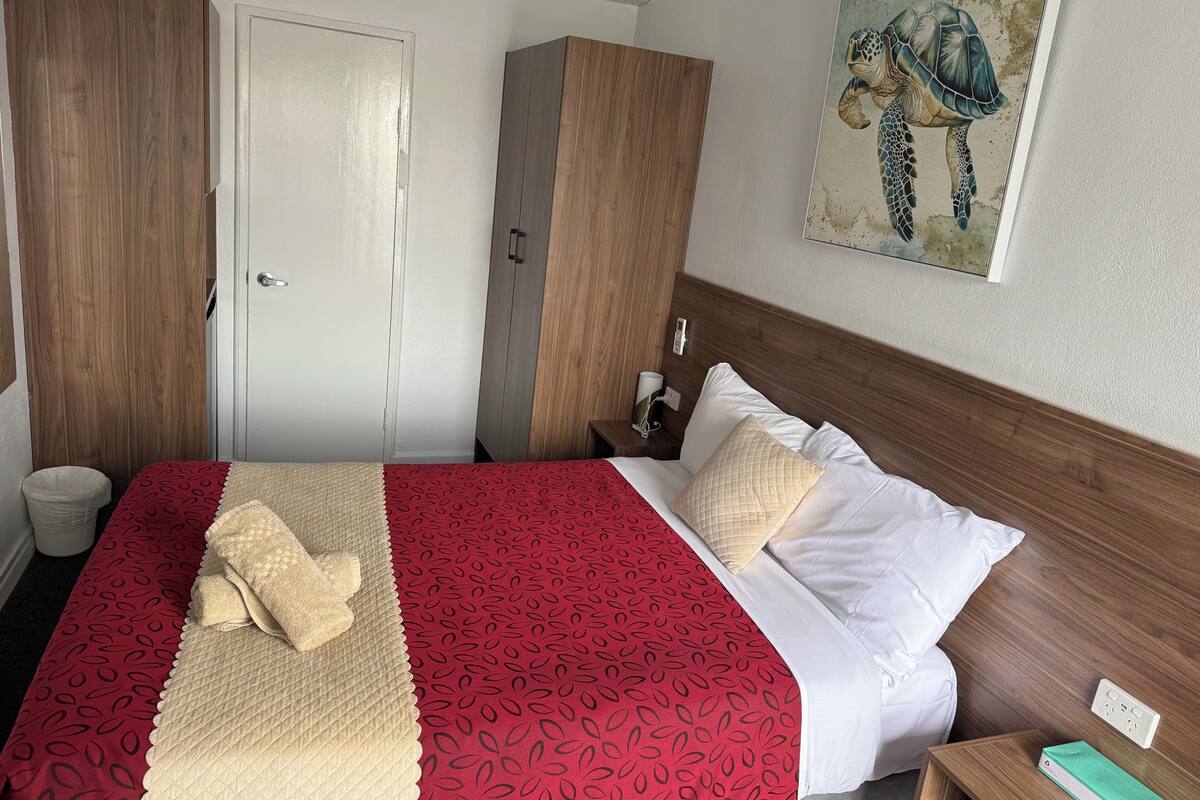 A hotel room with a bed, a wardrobe, a nightstand, and a painting on the wall.
