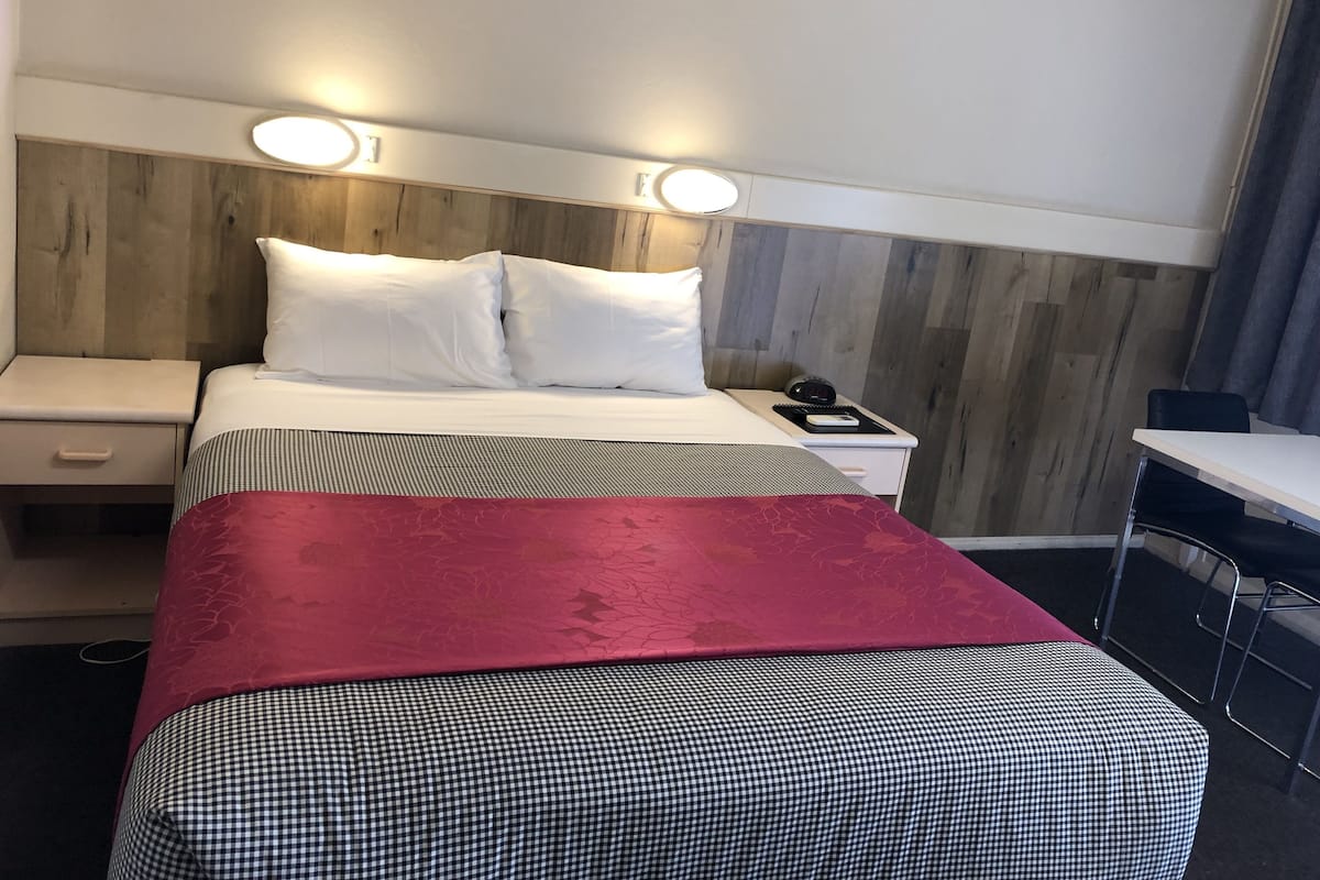 A hotel room with a bed, two bedside tables, a desk, and a chair.
