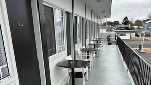 Un espacio de estar al aire libre cubierto con mesas y sillas, una puerta negra con el número 23, y vista a la calle.