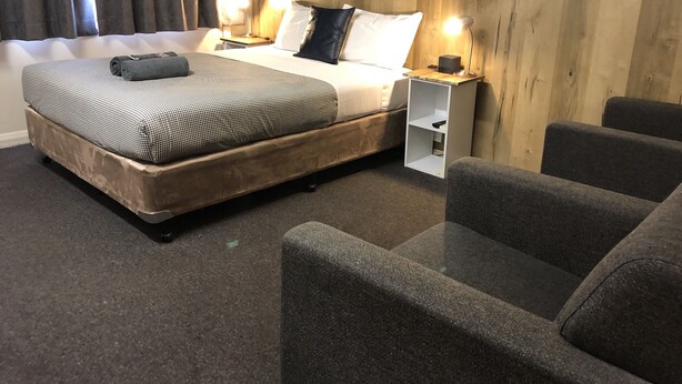 Habitación de hotel con una cama grande, dos mesitas de noche con lámparas, un estante pequeño y una zona de estar con dos sillones.