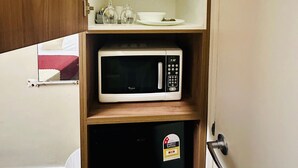 Una cocina compacta equipada con microondas, un refrigerador pequeño y una repisa con tetera y vasos.