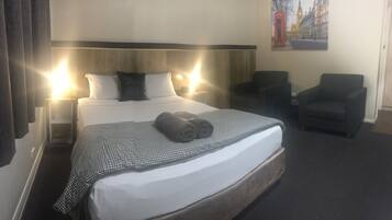 A hotel room with a bed, two chairs, a nightstand, and a painting on the wall.