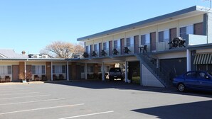 Un motel con aparcamiento, un corredor cubierto y una escalera que lleva a la entrada.