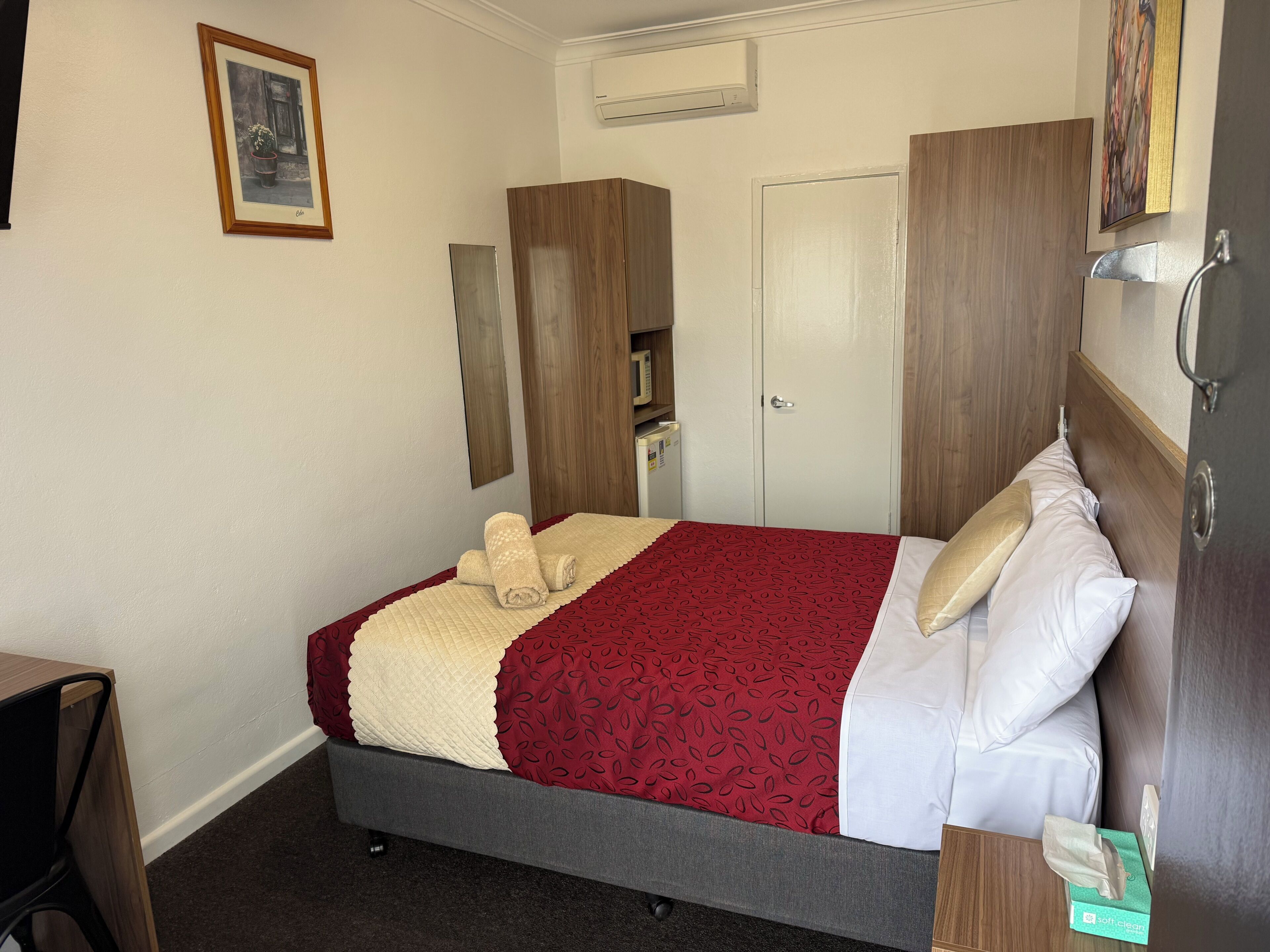 Quarto de hotel com cama, escrivaninha, guarda-roupa e ar condicionado.