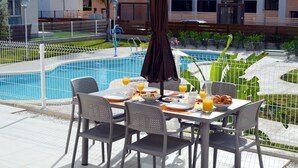 A dining table with chairs and breakfast items by a poolside. - Ground floor apartment, patio, pool views, free wifi, close to beach (Santiago de la Ribera)