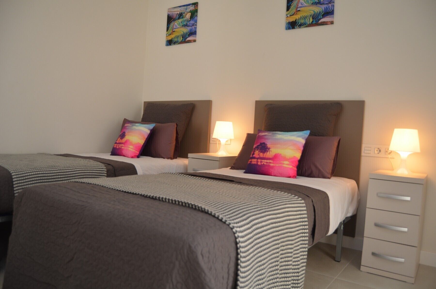 A hotel room with two single beds, each with a headboard, bedside tables, and lamps.