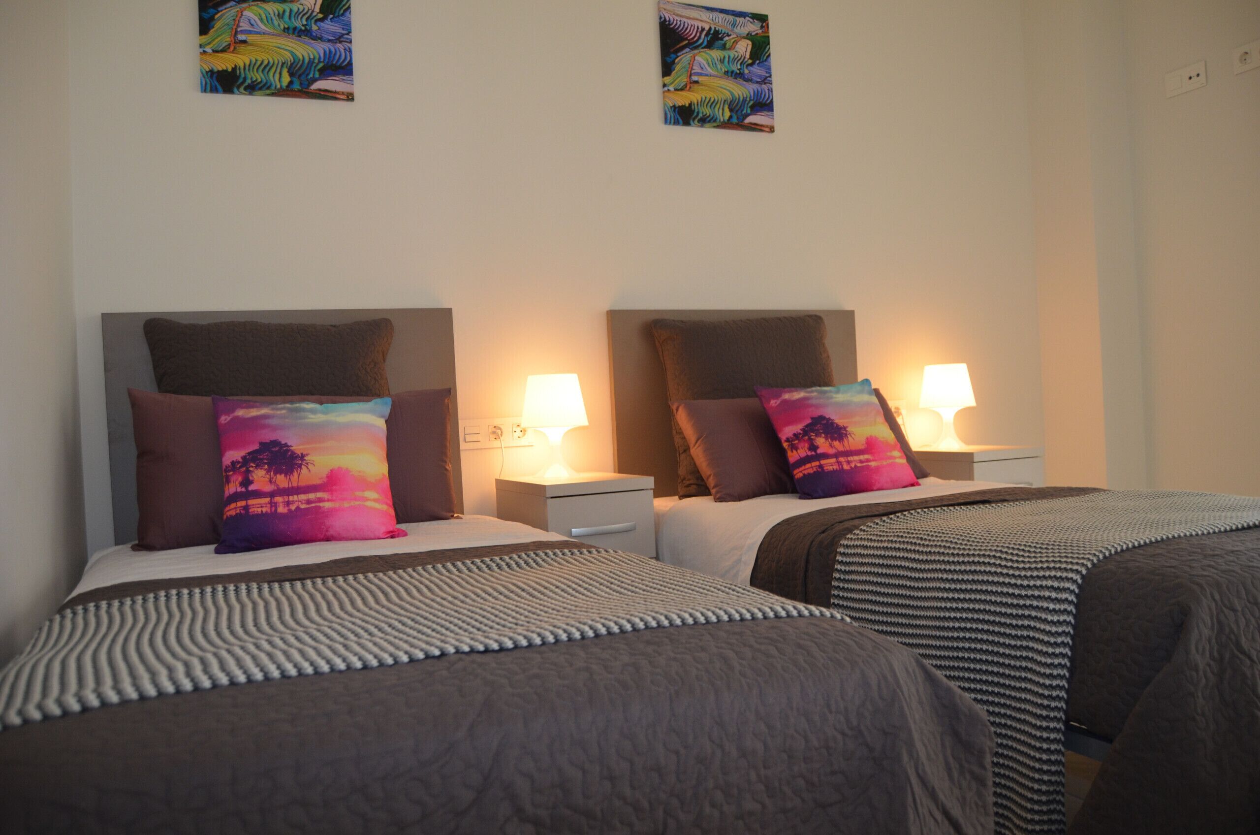 A hotel room with two beds, each with a pillow and a bedside lamp.