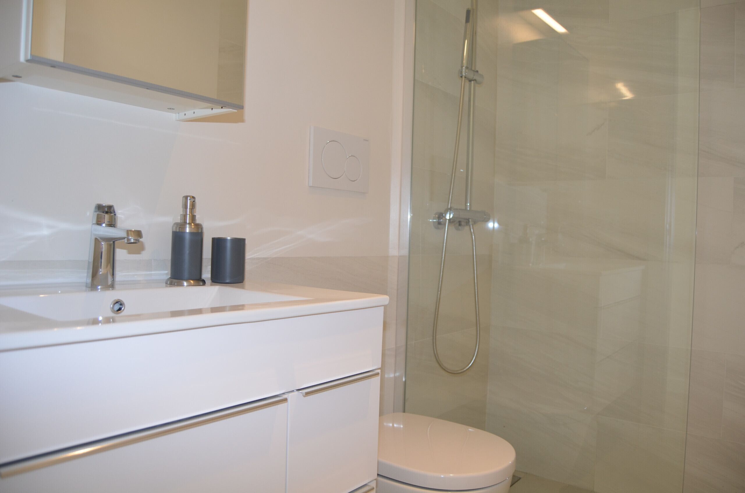 Un baño moderno con lavamanos, espejo y retrete blancos.
