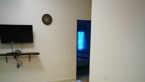 Una habitación con televisión de pantalla plana montada en la pared, alfombra estampada en el suelo y una cama con cortina azul al fondo.