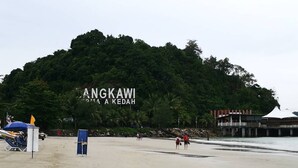 Una playa con un cartel grande que dice 'ANGKAWI' y un edificio al fondo.
