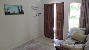 Una habitación con sofá, alfombra estampada, cuadro de veleros y puerta de madera que da al exterior.
