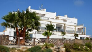 A modern multi-story building with balconies, surrounded by palm trees and a sandy landscape. - Ground floor apartment, patio, free wifi, sea view, BBQ (La Manga del Mar Menor)