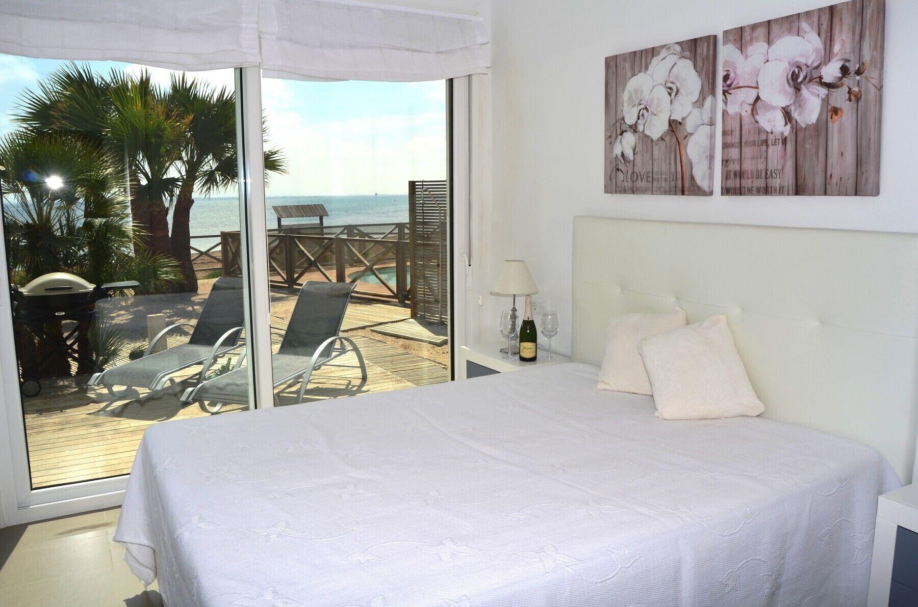 Une chambre avec un grand lit, une vue sur la plage et une terrasse avec des chaises et une table.
