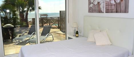 Une chambre avec un grand lit, une vue sur la plage et une terrasse avec des chaises et une table.