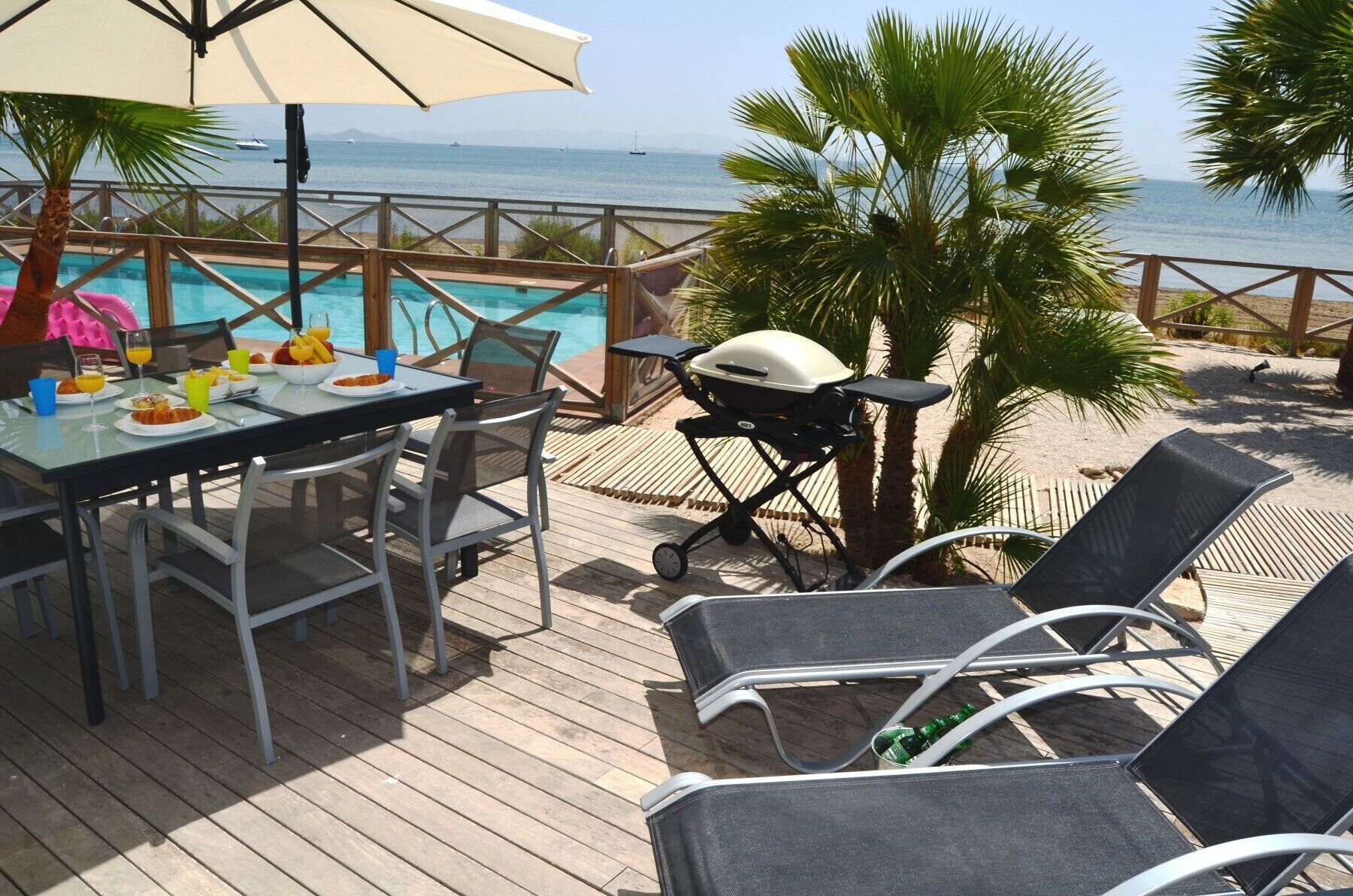 An outdoor dining area with a pool view, a grill, and lounge chairs.