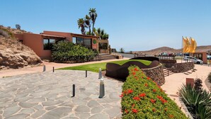 Un edificio moderno con fachada de vidrio, un camino de piedra y un jardín ajardinado con flores rojas.