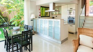 Una cocina moderna con una isla central, electrodomésticos integrados y un comedor con mesa y sillas de vidrio.