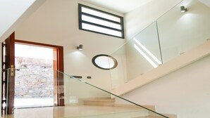 Una escalera moderna con barandillas de cristal, un muro de piedra en el exterior y un tragaluz arriba.