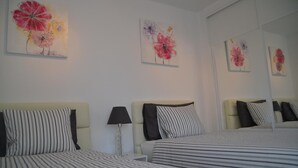 A hotel room with two beds, striped bedding, a bedside lamp, and floral artwork on the walls. - Home from home 2 bed luxury apartment with heated pool. 118 (Puerto del Carmen)