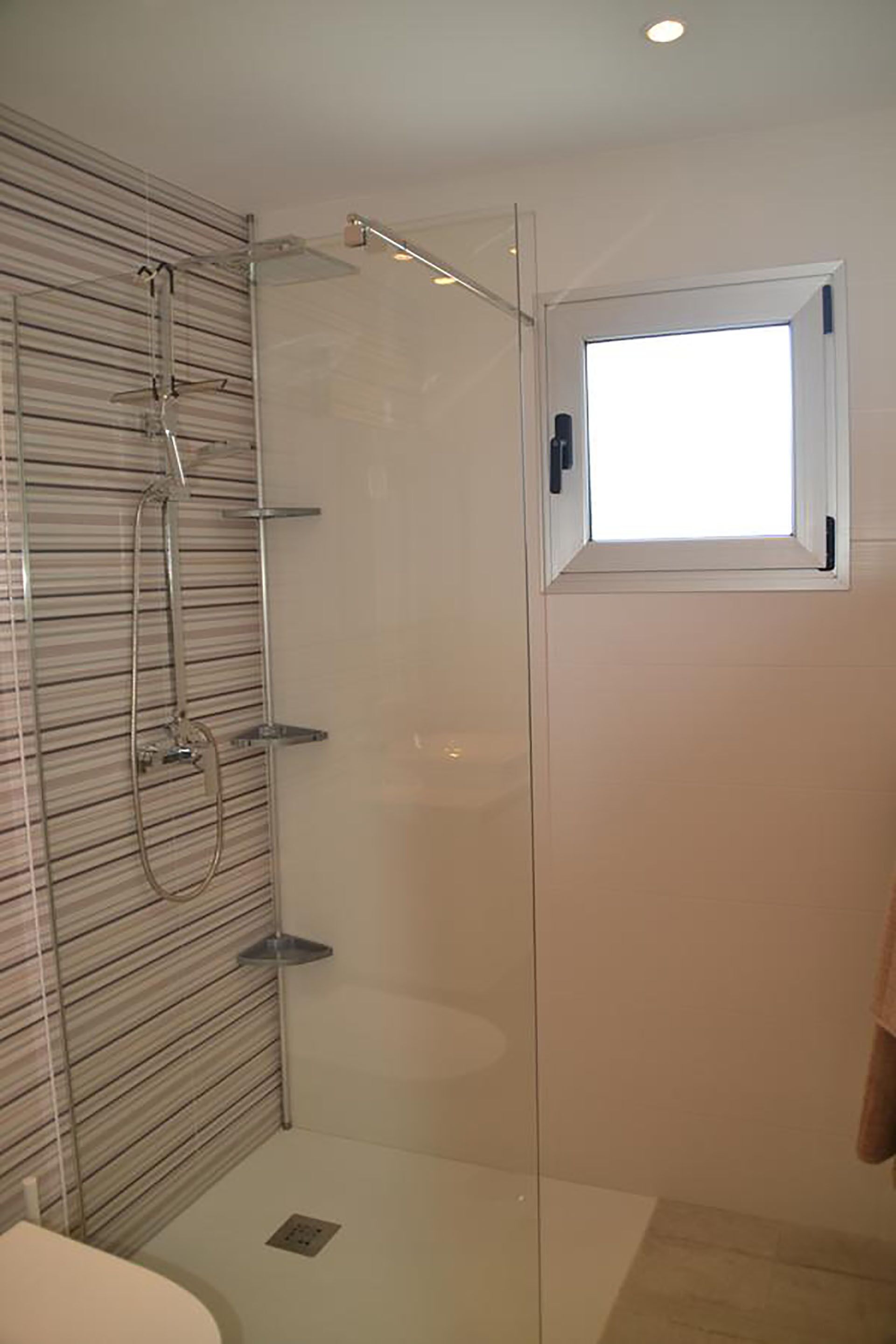 A modern bathroom with a glass shower enclosure, a small window, and a towel rack.