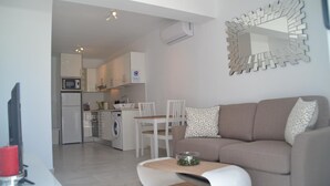 A modern living room with a sofa, a coffee table, and a dining area with chairs. There is a kitchen visible in the background with cabinets and appliances. - Home from home 2 bed luxury apartment with heated pool. 118 (Puerto del Carmen)
