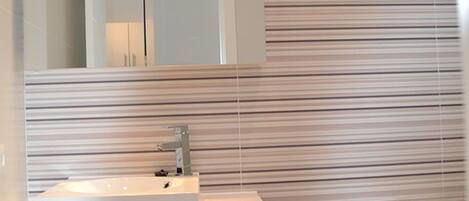 Een moderne badkamer met een gestreept wandontwerp, een grote spiegel, een wit wastafelmeubel en een toilet.
