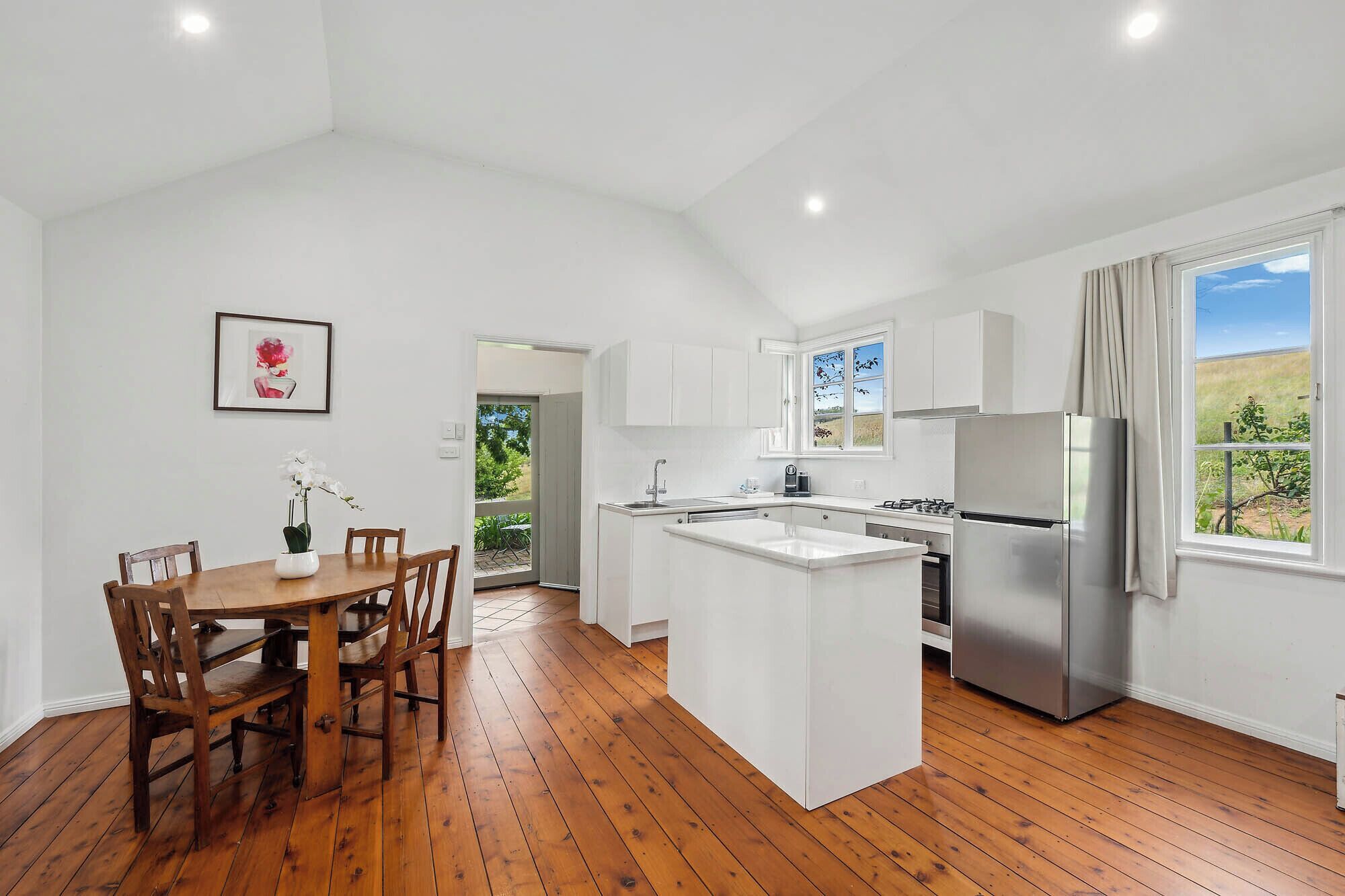 A modern kitchen with white cabinets, a stainless steel refrigerator, and a wooden dining table with chairs.