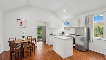 A modern kitchen with white cabinets, a stainless steel refrigerator, and a wooden dining table with chairs.