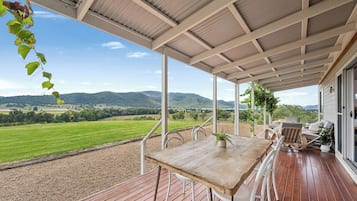 Een overdekt terras met een tafel en stoelen, met uitzicht op een schilderachtig landschap met heuvels en velden.