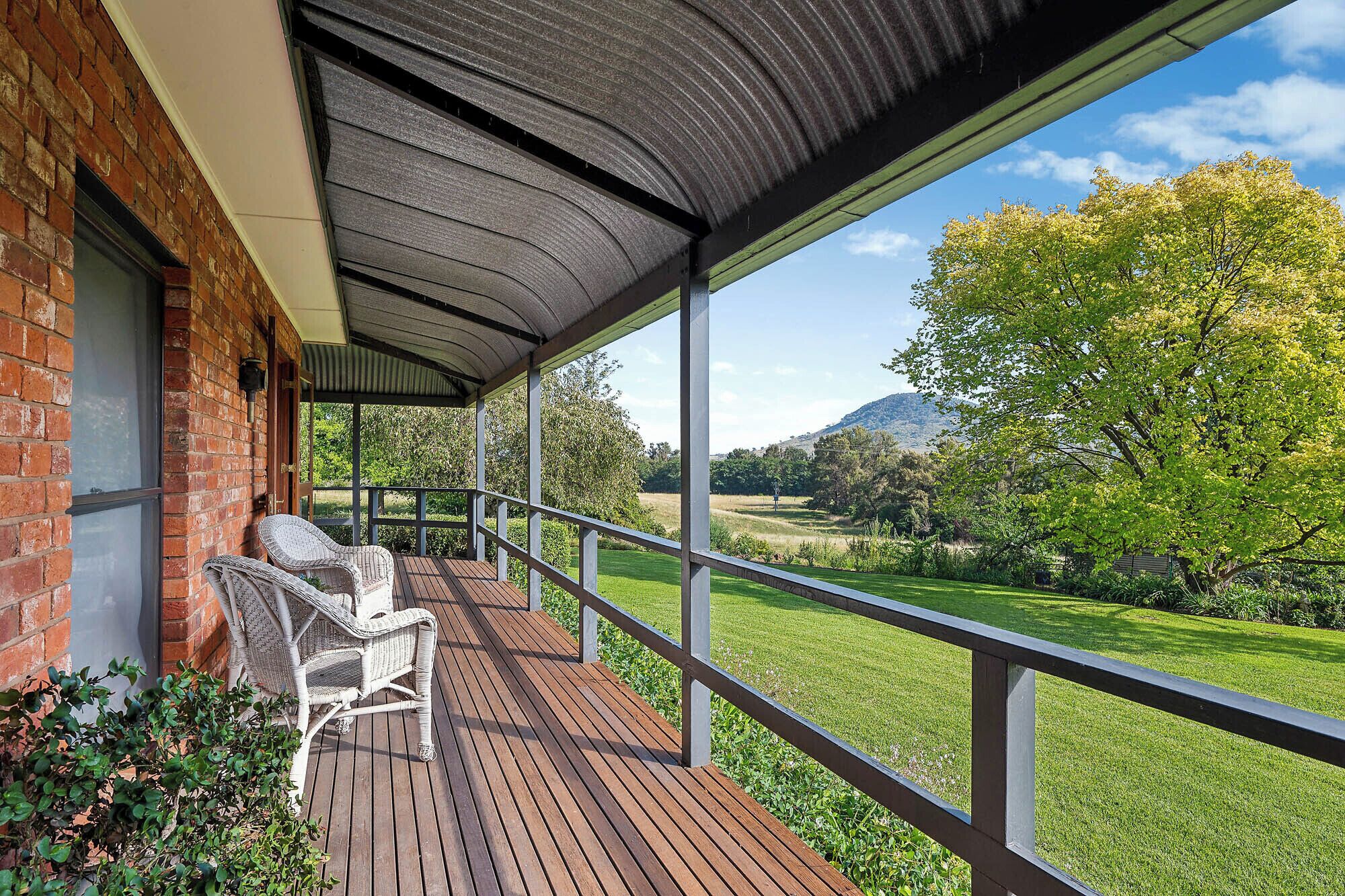 Un espacio al aire libre techado con terraza de madera, sillas de mimbre y vista a un paisaje verde con árboles y colinas.