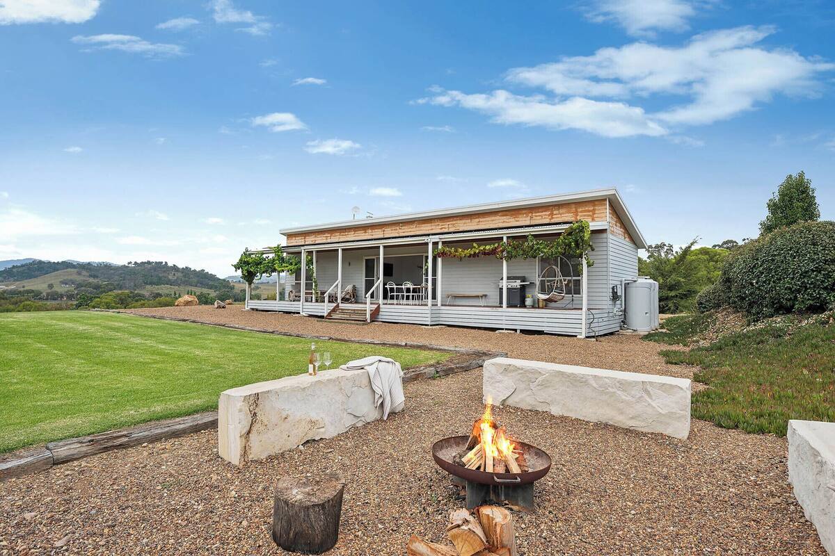 Une maison moderne dotée d’un porche abrité, d’un foyer extérieur et offrant une vue sur la campagne.
