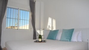 Une chambre à coucher avec un grand lit, une fenêtre avec des barreaux, une table de chevet avec une bouteille et des verres, et une lampe.