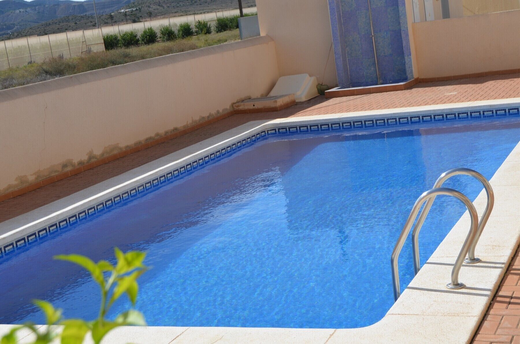 Une piscine à l’eau d’un bleu limpide, avec une échelle en métal et un bord carrelé.