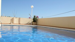 Une piscine aux eaux claires, bordée de carreaux, un lampadaire blanc et un pot de fleurs orné de fleurs roses.