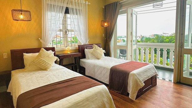 A hotel room with two beds, a desk, and a balcony with a railing. - fullhouse hoian (Da Nang)