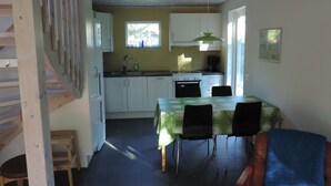 A compact kitchen with white cabinets, a dining table with chairs, and a staircase leading to another level. - Beachfront - Österlen (Degeberga)
