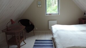 A small, cozy attic bedroom with a sloped ceiling, a single window with a view of trees, a bed, a chair, and a table. - Beachfront - Österlen (Degeberga)