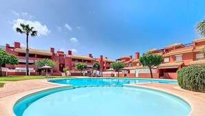 Une piscine entourée de bâtiments rouges dotés de balcons, un ciel bleu clair et quelques espaces verts.