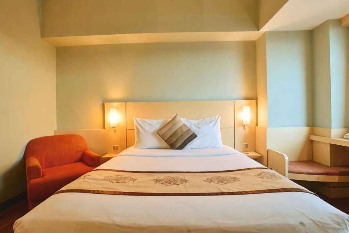 Una habitación de hotel con una cama, dos lámparas de noche, una mesita de noche, una silla y una pequeña mesa.