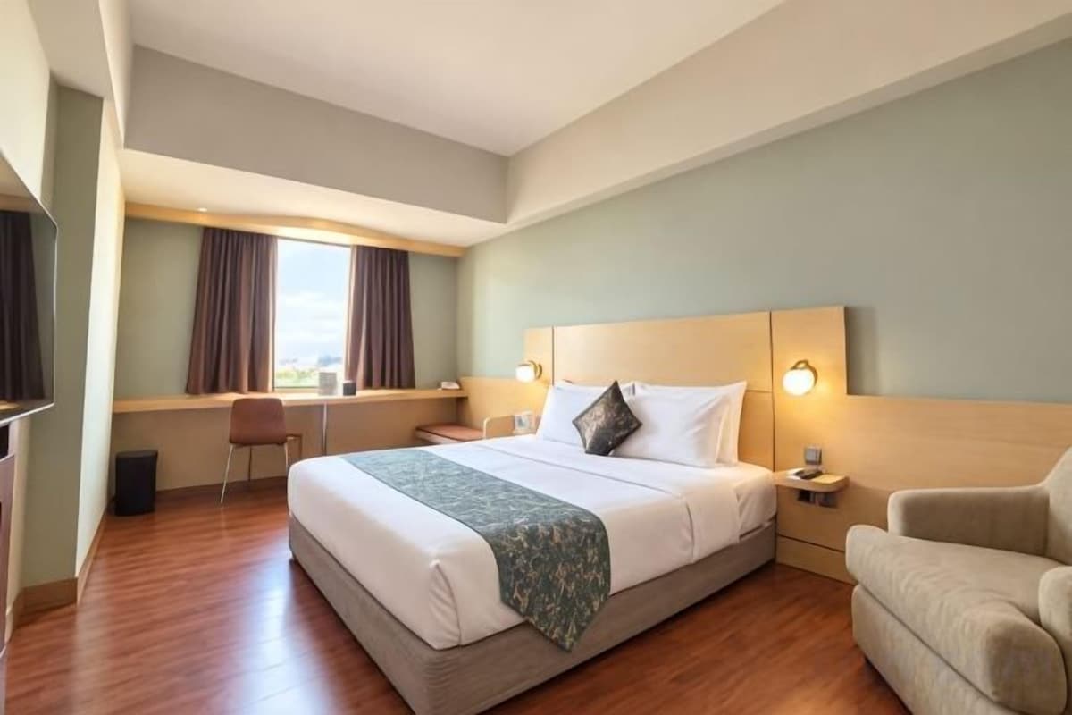 A hotel room with a bed, bedside table, lamp, chair, and a desk with a chair.